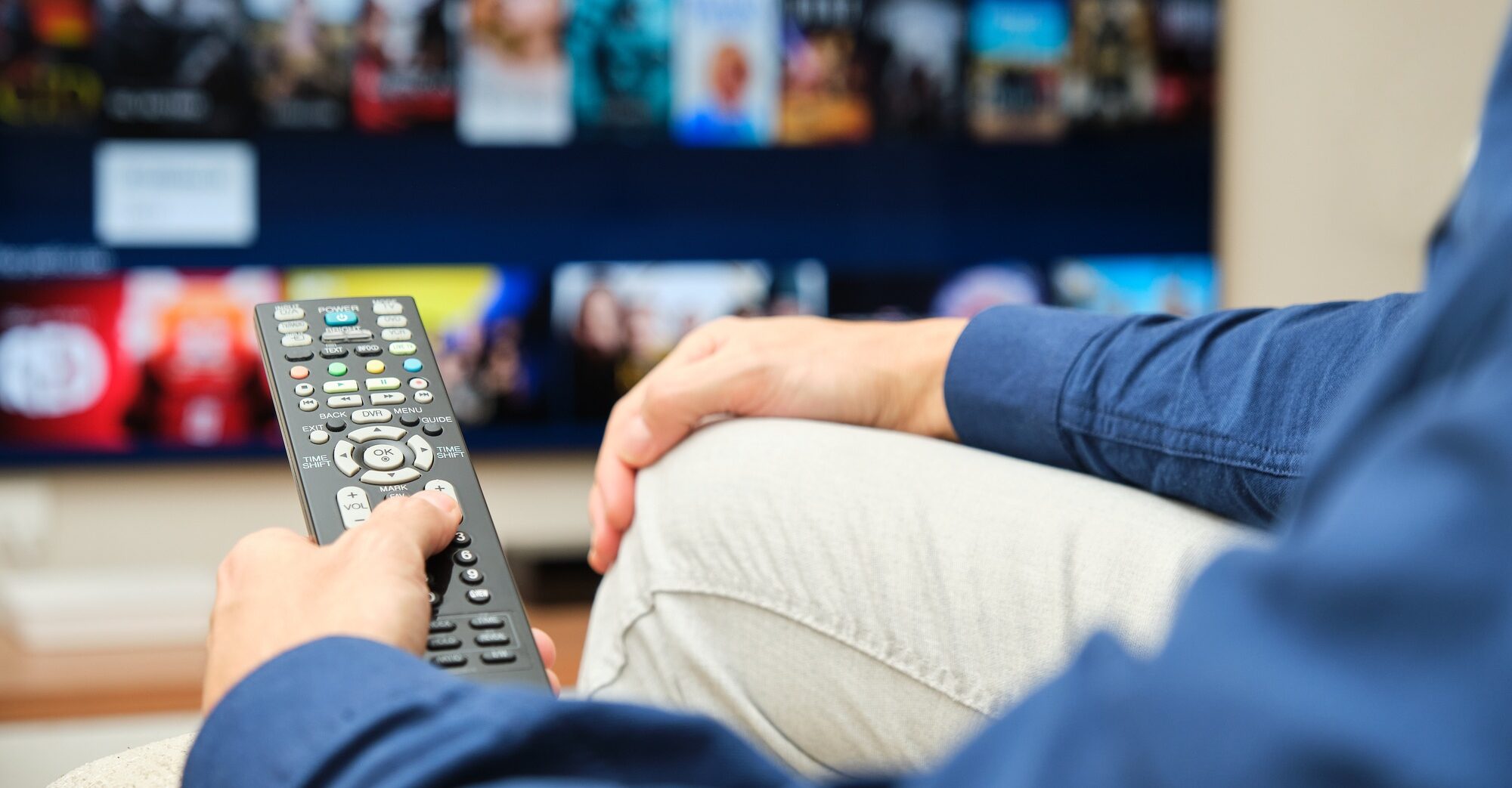 unrecognizable man sitting on the sofa looking on the tv for content on a streaming platform